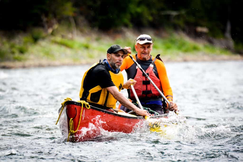 Two men canoeing in rapids, bowman cross drawing