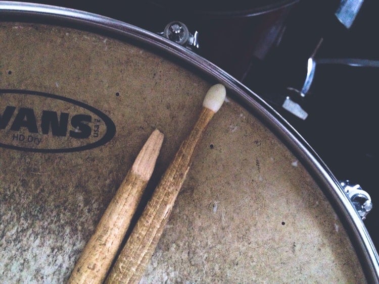 Two drum sticks laying on a snare drum head, one of the sticks is broken off at a severe angle